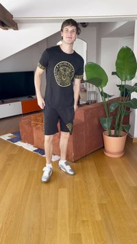 Juoda marškinėlių su auksiniu liūto grafiku ir raštuotais rankovėmis, derinami su juodais šortais su auksiniais akcentais. Sidabriniai sportiniai bateliai.