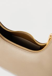 Μπεζ δερμάτινο τσαντάκι Calvin Klein με χρυσό φερμουάρ μερικώς ανοιχτό, που αποκαλύπτει το εσωτερικό τσέπη με το λογότυπο Calvin Klein.