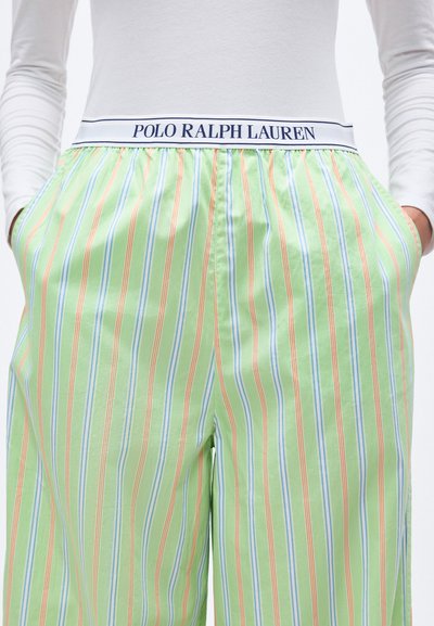 Άτομο που φοράει ανοιχτοπράσινο παντελόνι με ρίγες και τσέπες, με λευκή ζώνη μέσης με την ετικέτα "Polo Ralph Lauren", σε συνδυασμό με λευκό μακρυμάνικο τοπ.