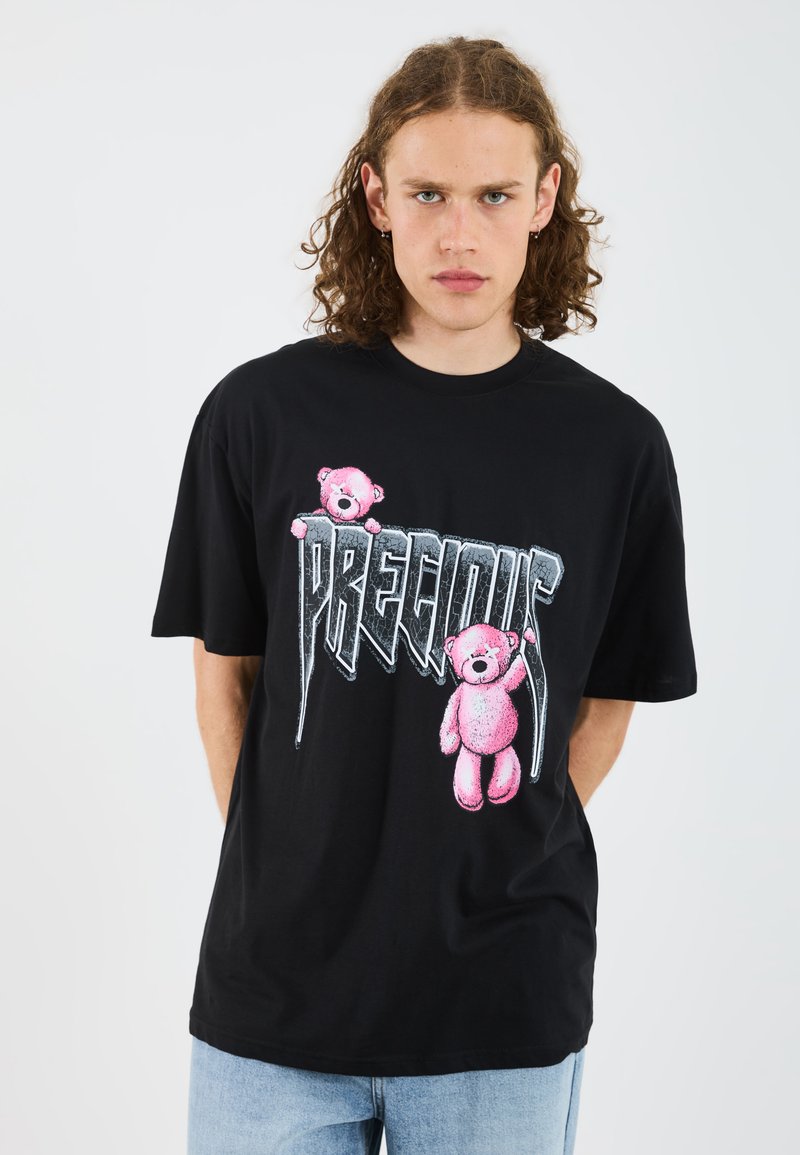 T-shirt in cotone nero con grafiche di orsetti rosa e testo "PRECIOUS" in font audace e stilizzato. Maniche corte e vestibilità comoda.