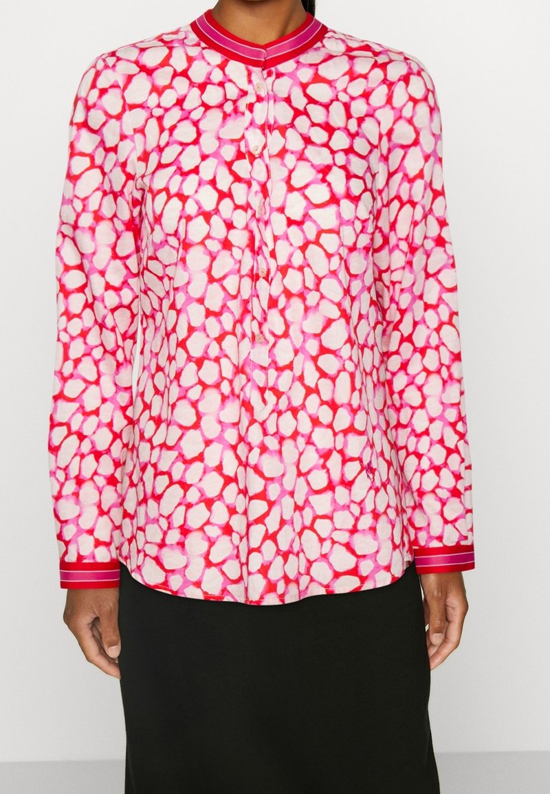 Camicia a maniche lunghe di colore rosa con un motivo astratto di forme bianche irregolari, dotata di un colletto e polsi solidi rosa con accenti rigati.