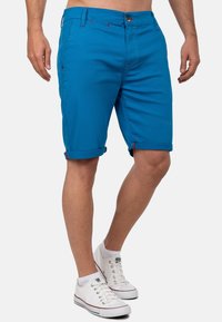 Heldere blauwe katoen shorts met opgerolde zomen, contrasterende rode stiksels en een sluiting met een knoop aan de voorkant. Draag ze met witte sneakers.