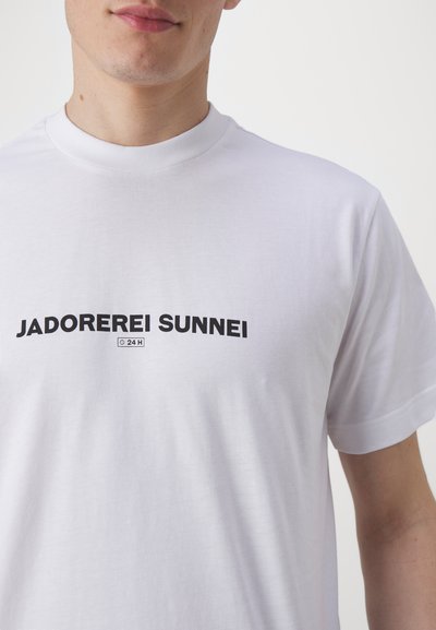 Valge puuvillane T-särk, millel on must tekst "JADOREREI SUNNEI" ja väike "24 H" logo. Lühikesed varrukad ja ümar kaelus. Sile tekstuur.