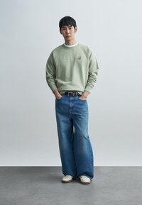 Φιστικί φούτερ με ριμπ υφή, άνετη εφαρμογή; μπλε παντελόνι ψηλόμεσο με φαρδιά μπατζάκια; λευκά αθλητικά παπούτσια; ζώνη στη μέση.