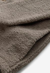 Weicher, strukturierter brauner Stoff mit einer flauschigen Oberfläche, der zudem abgesteppten Kanten und fallende Falten aufweist, wodurch seine Wärme und Dicke betont werden.