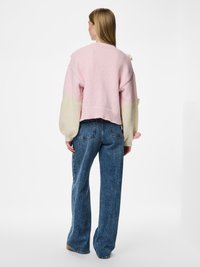 Πλεκτό πουλόβερ σε ροζ και κρεμ με κοντό σχέδιο, υφασμένα μπαλόν μανίκια και διακοσμητικά πομ πομ. Φορεμένο με ψηλόμεσα μπλε τζιν.