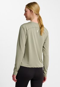 Langärmliges Sportshirt in Hellgrün, aus glattem, leichtem Stoff gefertigt. Verfügt über einen runden Ausschnitt und ein dezentes Logo auf der Rückseite.