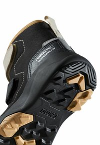 Schwarzer wasserdichter Schuh mit strukturiertem Obermaterial, verstärkten Akzenten und einer robusten Gummisohle mit multidirektionalen Profilen und einer tanfarbenen Laufsohle.