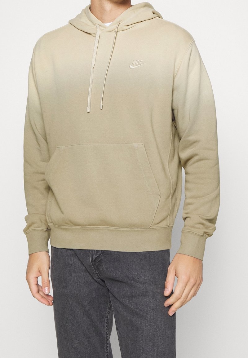 Felpa beige con sfumature, dotata di tasca frontale, cappuccio con coulisse e logo Nike ricamato. Il materiale è morbido, con polsini e orlo a costine.