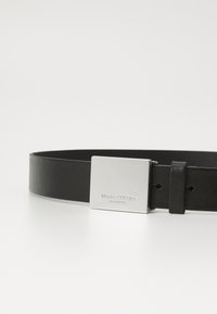 Czarny skórzany pasek z prostokątną metalową klamrą w kolorze srebrnym. Klamra posiada wygrawerowaną nazwę marki. Gładka tekstura, minimalistyczny design.