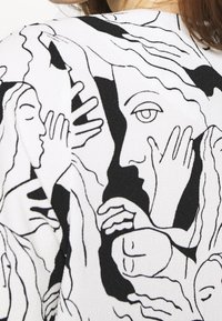Tessuto bianco con un design astratto nero di volti e mani con capelli fluenti, che mostra un lavoro di linee intricati e contrasti audaci.