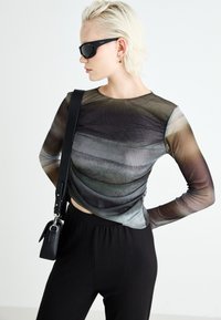 Haut à manches longues en tissu transparent multicolore affichant des rayures horizontales en dégradé. Assorti à un pantalon noir à côtes et un petit sac.