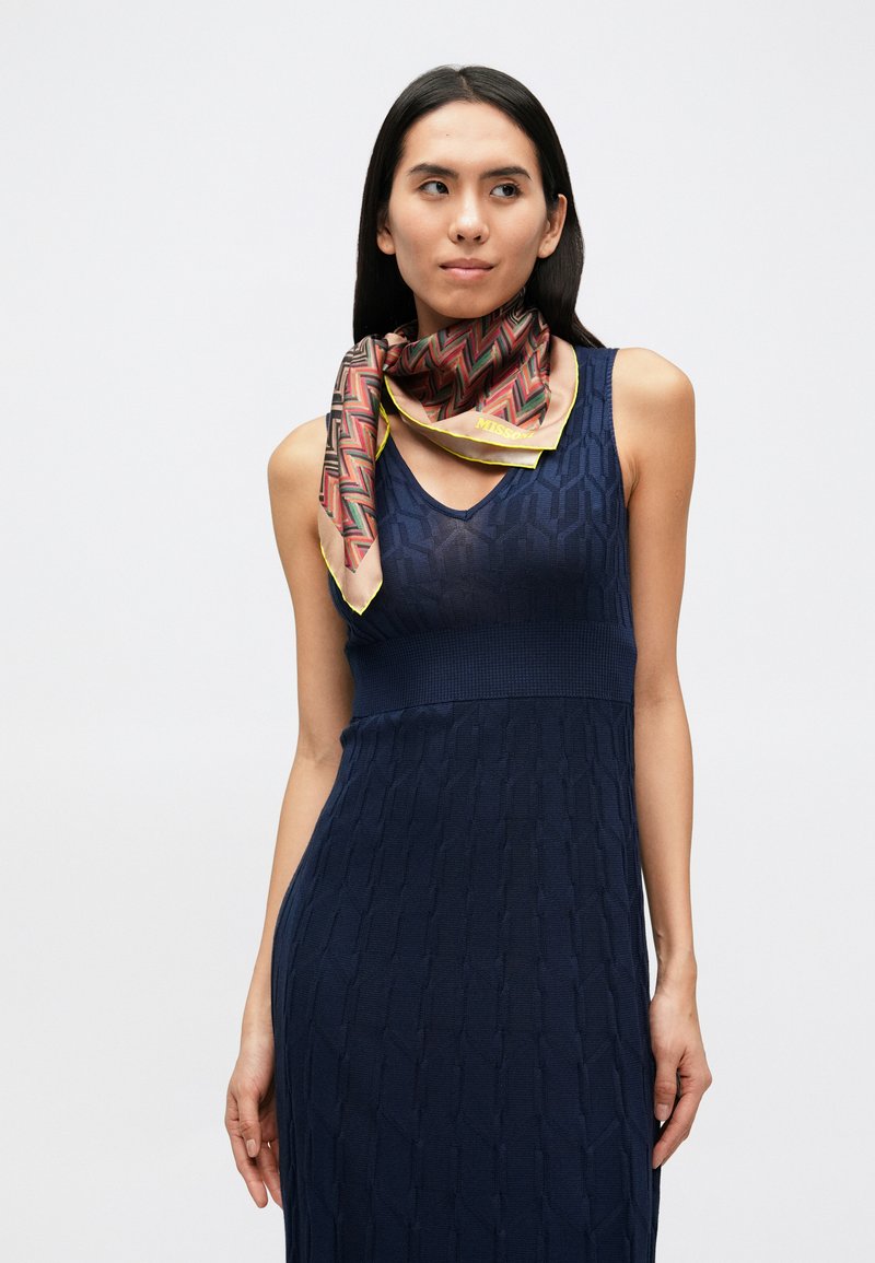 Sciarpa di seta con motivo geometrico a zigzag in rosso, marrone e giallo su sfondo crema, bordata con rifinitura gialla.