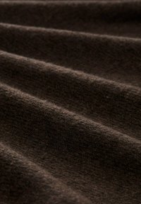 Close-up van zachte, donkerbruine stof met een pluizige textuur en gelijkmatig verdeelde plooien die een golfachtig patroon creëren.