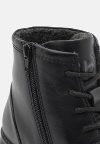 Bottine en cuir noir avec fermeture éclair latérale, lacets et doublure douce en polaire à l'intérieur du col.