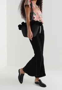 Blommig rosa t-shirt, svarta utsvängda byxor med vit sömnad, svart vävd väska med pom-poms och svarta slip-on skor.