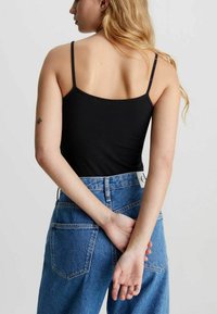 Camiseta sin mangas negra con tirantes finos, combinada con unos vaqueros de mezclilla azul de tiro alto que presentan un diseño clásico de cinco bolsillos y costuras visibles.