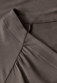 Hnědá látka se soft-touch textura s designem do V. Na krku je sbírané zdobení a čisté zakončení na okrajích.