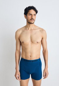 Blue stretch boxer briefs feature an elastic waistband with "BJÖRN BORG" branding. The fabric has a smooth, matte texture.