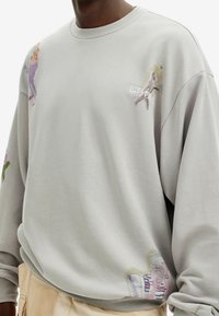 Sudadera gris claro con diseños abstractos coloridos y logo bordado en el pecho. Presenta un cuello redondo y un ajuste relajado.