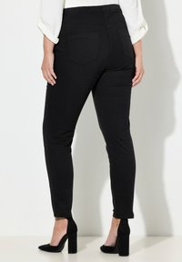 Czarne rozciągliwe spodnie o wąskim kroju, z wysokim paskiem, tylnymi kieszeniami i nogawkami do kostek, zestawione z czarnymi butami na obcasie.