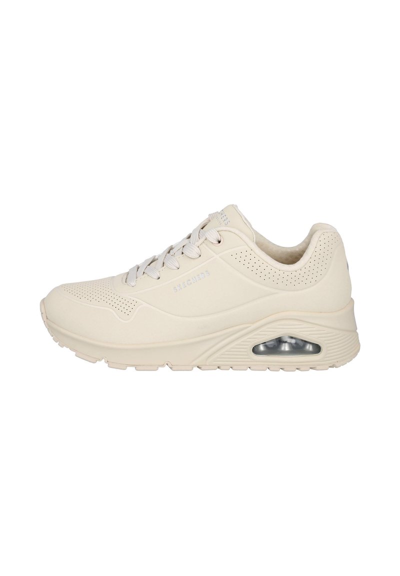 Zapatilla deportiva beige con un upper texturizado, perforaciones para transpirabilidad, cordones planos y amortiguación de aire visible en el talón.