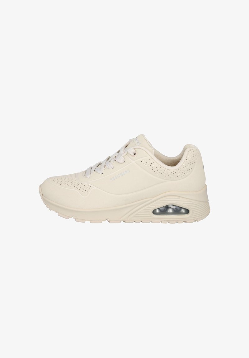 Zapatilla deportiva beige con un upper texturizado, perforaciones para transpirabilidad, cordones planos y amortiguación de aire visible en el talón.