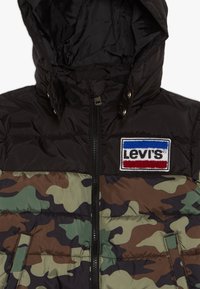 Polstret jakke med sort hætte og camouflage-mønster i grøn og brun. Lynlås foran med Levi's-mærke på brystet.