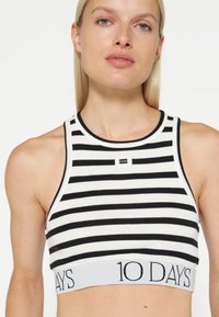 Gestreept crop top in zwart en wit, met een solide band met het label "10 DAGEN." Geribbelde textuur en ronde halslijn.