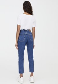 Jean en denim bleu taille haute avec une coupe droite, doté de deux poches arrière doubles et d'un patch en cuir de marque sur la ceinture.