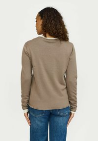 Pruun pikkade varrukatega sviiter ribatud tekstuuriga, ümmargune kaelus ja kontrastsed heledat hallid mansetid, kombineerituna siniste laialdaselt istuvate teksadega.