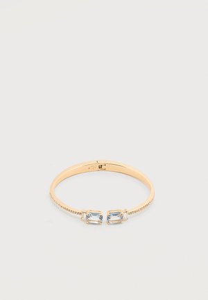 Náramok na zápästie v zlatej farbe s dvoma obdĺžnikovými svetlomodrými drahokamami tvárou v tvár a malými kryštálmi pozdĺž pásma.