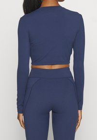 Top corto de manga larga en color marino con diseño ajustado, textura suave y cuello redondo, combinado con leggins de cintura alta a juego.
