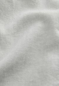 Tissu en lin gris clair avec une surface légèrement texturée, présentant des plis et des rides subtils, mettant en valeur son tissage naturel.