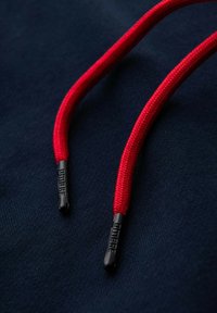 Czerwone sznury teksturowane z czarnymi plastikowymi końcówkami na ciemnoniebieskim tle, ukazujące kontrastujący design.