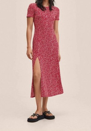 Kobieta ubrana w czerwoną, kwiecistą, krótką sukienkę midi z rozporkiem do uda, w połączeniu z czarnymi sandałami na platformie.