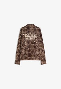 Brown checked shirt with a soft texture, featuring printed text "SOFTNESS WRAPPED IN STEEL" and bird motifs on the back.
