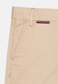 Pantaloni in cotone beige dal design elegante, con tasca laterale e un piccolo dettaglio a strisce rosse, bianche e blu in vita.