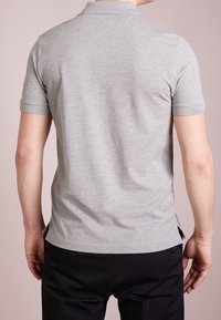 Polo gris à manches courtes, avec un col classique, une coupe droite et des fentes sur les côtés. Fabriqué en matériau doux et léger.