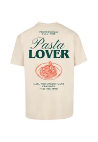 Crème katoenen t-shirt met groene tekst en een oranje pasta graphic. Achterzijde toont "Professionele Full-Time Pasta Liefhebber" en contactgegevens.