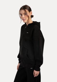 Czarna bluza zip-up wykonana z miękkiego materiału. Posiada dużą kaptur, przednie kieszenie oraz małe logo na piersi. Luźny krój.