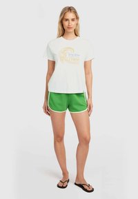 White short-sleeve t-shirt with graphic design at front, paired with green athletic shorts featuring white side stripes and a textured fabric.