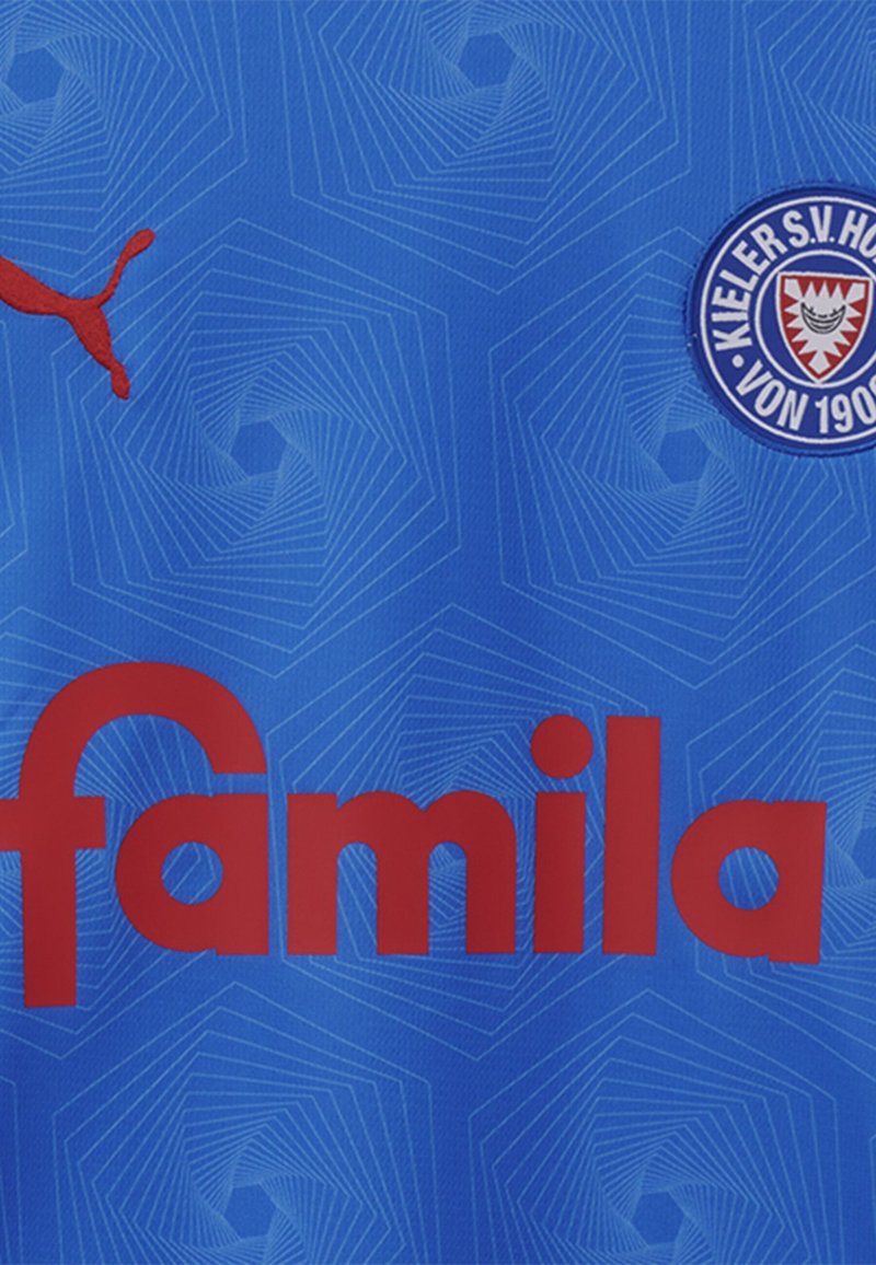 Modra športna majica z rdečim logotipom "famila", vzorčastim ozadjem in rdečim logotipom Puma. Vključuje okrogel ekipni znak na desni strani.