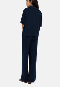 Granatowy dzianinowy top z krótkimi rękawami i luźnym krojem, zestawiony z szerokimi granatowymi spodniami, prezentującymi gładką teksturę i prosty design.