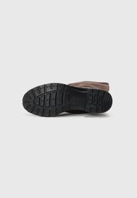 Semelle d'une botte marron orientée vers le haut, montrant un motif noir avec de profonds sillons et le nom de marque "ECCO" embossé au centre.