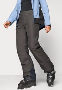 Μαύρο παντελόνι σκι με άνετη εφαρμογή, φτιαγμένο από αδιάβροχο υλικό. Διαθέτει τσέπες και ενισχυμένα τμήματα γύρω από τους αστραγάλους. Συνδυάζεται με μπότες σκι.