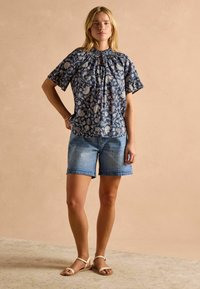 Námornícky modrý top s kvetinovým vzorom, krátkymi rukávmi a výrezom na krku, skombinovaný s svetlými denním šortkami a plochými sandálmi.