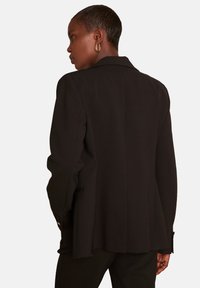 Blazer nero con design strutturato, rever a lancia e spacchetto singolo. Presenta due tasche laterali e maniche lunghe su misura.