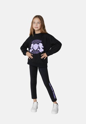 Zwarte sweatshirt met paarse "Unicorn Academy" graphic, gecombineerd met zwarte leggings met de tekst "Find Your Unicorn" en witte sneakers.