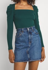 Grön randig långärmad topp med fyrkantig halsringning, kombinerad med en blå denim minikjol med knäppning fram och sidofickor.